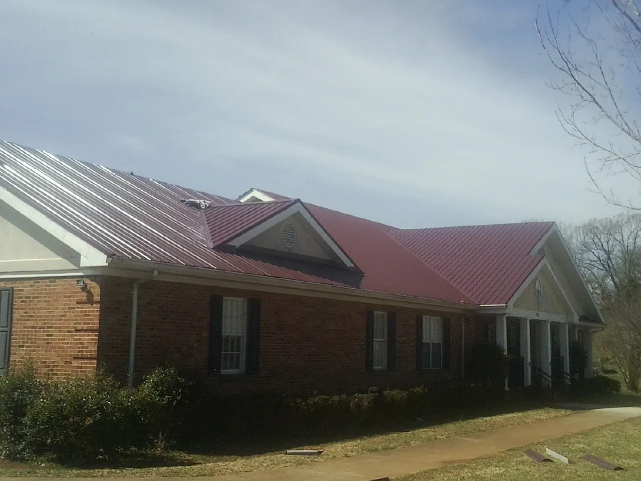 Red metal roof with gabled entries on a long brick building, from a Hail Damage Roof Repair job in Lake George