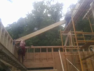 Carpenter raising a rafter beam on a new second story frame in Lake George