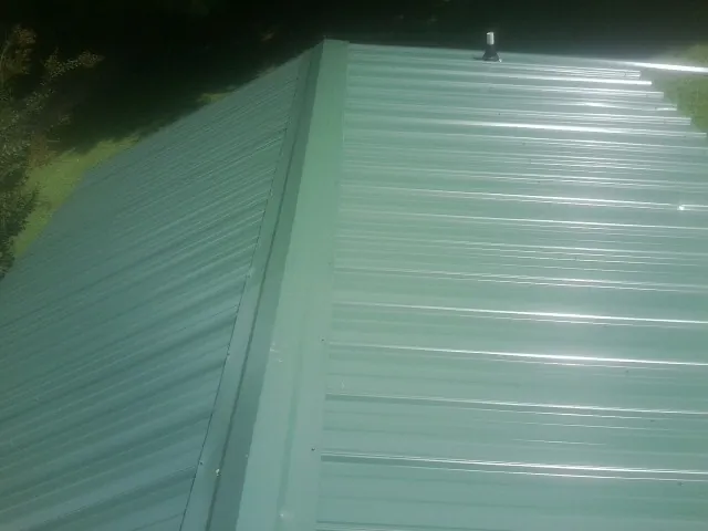 New green metal panels meeting at the ridge of a roof — Flat Roof Repair work by our crew in Lake George