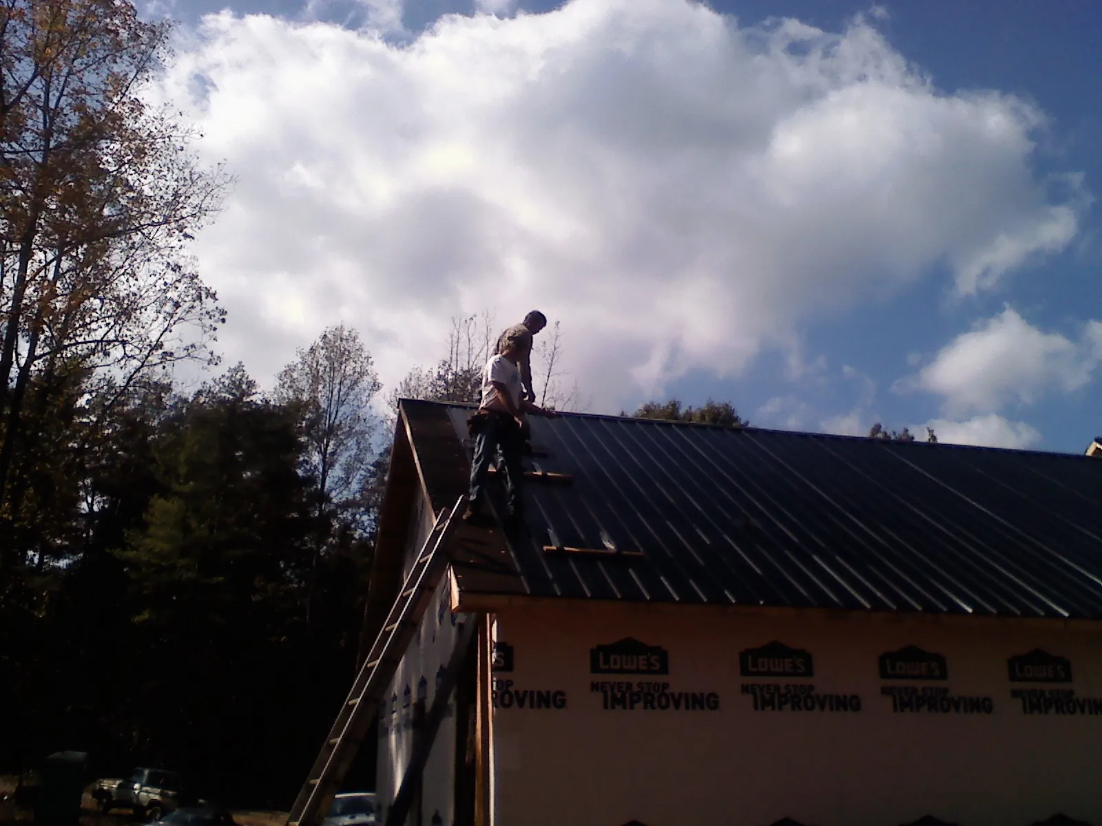 Roofer fastening dark metal panels high against a cloudy sky, from a Roof Inspection job in Lake George