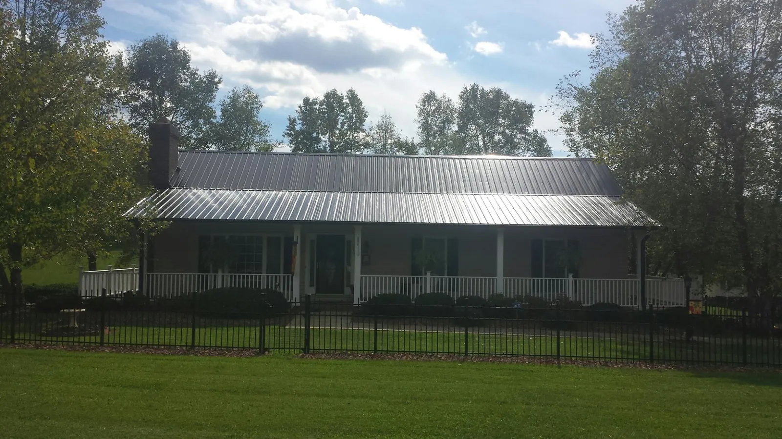 Gray metal roof on a brick ranch with a full width front porch — Gutter Guard Installation work by our crew in Lake George
