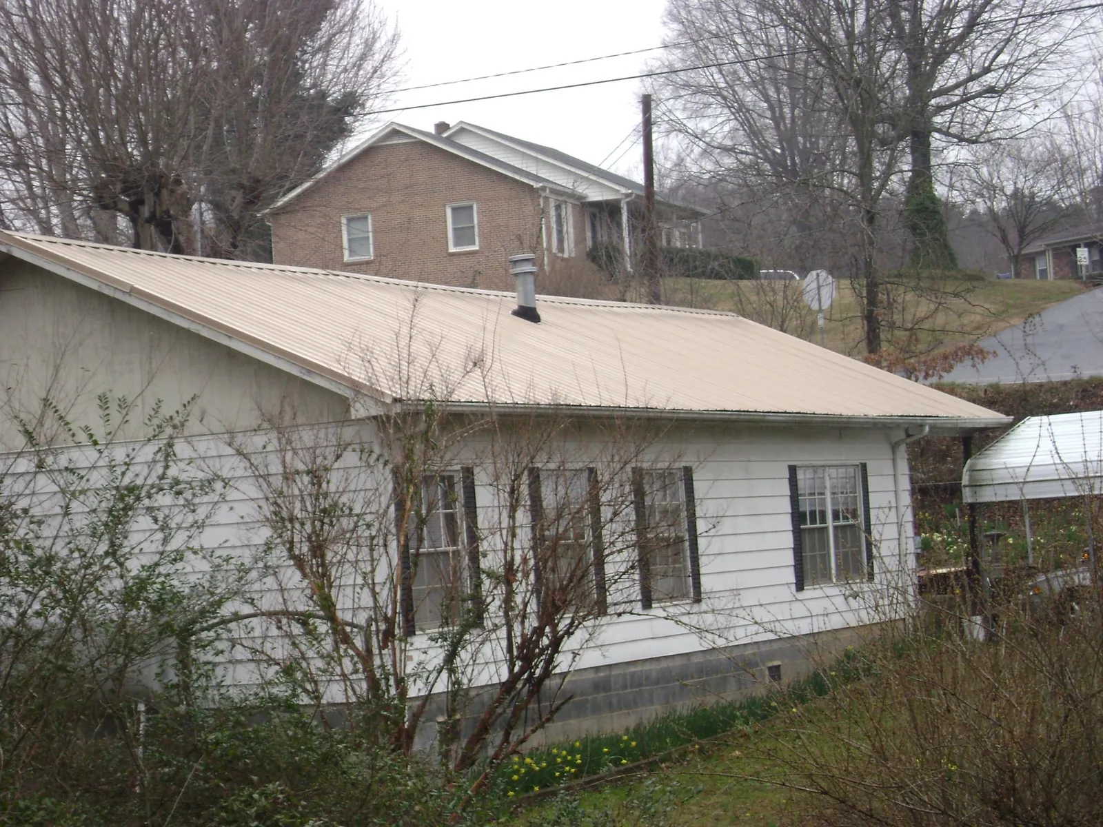 Tan metal roof on a white sided house set into a hillside — Commercial Roofing by Roofing Brothers in Lake George